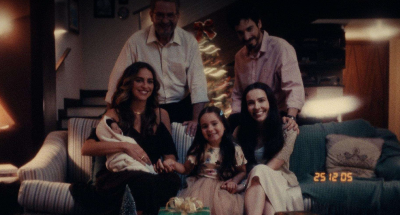 Família reunida em clima natalino, conversando à mesa, com expressões de afeto e reflexão