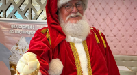 Papai Noel sorrindo com sorvete na mão na Cacimba Sorvetes, em ambiente iluminado e festivo que evoca a atmosfera mágica do Natal.