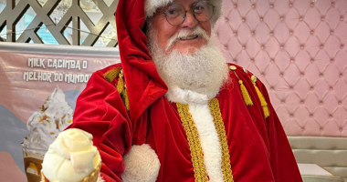 Papai Noel sorrindo com sorvete na mão na Cacimba Sorvetes, em ambiente iluminado e festivo que evoca a atmosfera mágica do Natal.