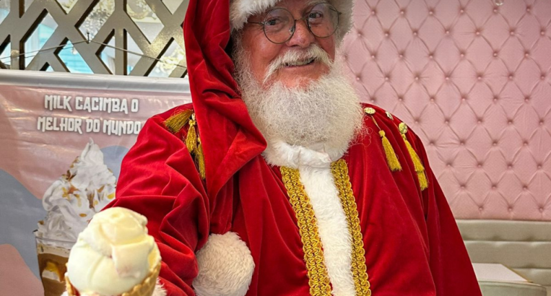 Papai Noel sorrindo com sorvete na mão na Cacimba Sorvetes, em ambiente iluminado e festivo que evoca a atmosfera mágica do Natal.