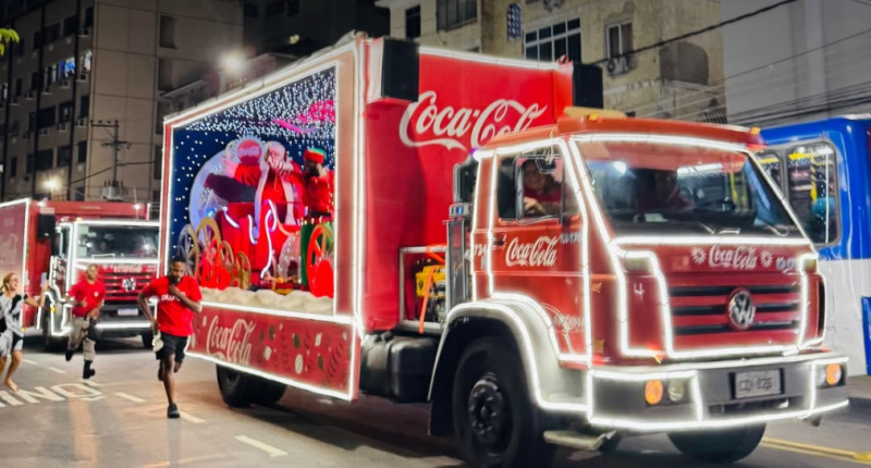 Caminhões iluminados da Caravana de Natal da Coca-Cola passando por avenida à noite