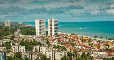 Vista aérea de praia brasileira movimentada no verão, com turistas aproveitando o clima de férias
