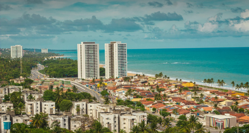 Vista aérea de praia brasileira movimentada no verão, com turistas aproveitando o clima de férias