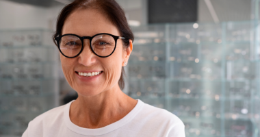 Mulher madura em ambiente iluminado segurando seus óculos, em cena suave que simboliza cuidado, bem-estar e atenção à saúde ocular após os 50.