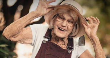 Idosa sorrindo em parque arborizado,transmitindo bem-estar, leveza e conexão com a natureza.