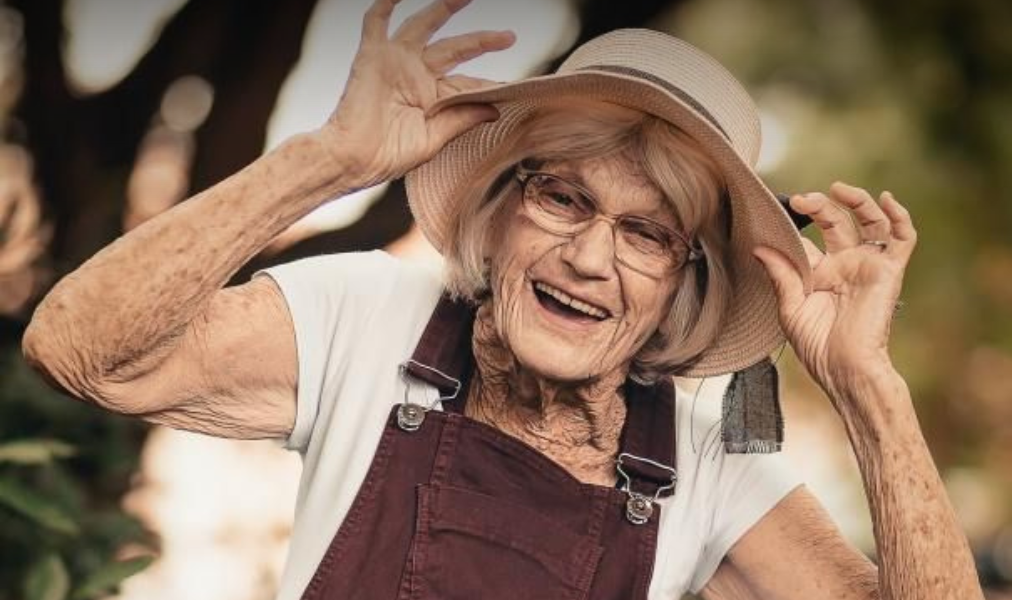 Idosa sorrindo em parque arborizado,transmitindo bem-estar, leveza e conexão com a natureza.