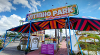 Fachada colorida do Vitinho Park montado no Bosque dos Ipês, com brinquedos em movimento e famílias aproveitando a estreia ao entardecer.