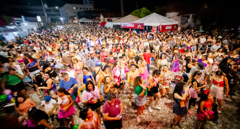 Foliões diversos dançando ao som do trio elétrico na Esplanada Ferroviária durante o Capivara Blasé, com crianças participando do cortejo