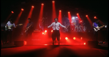 Banda Lagum se apresentando ao vivo em palco iluminado, com público vibrando em show com atmosfera moderna e luzes coloridas