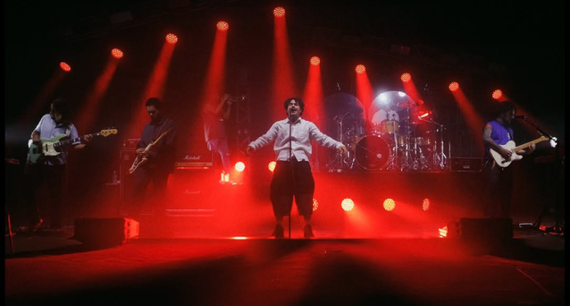 Banda Lagum se apresentando ao vivo em palco iluminado, com público vibrando em show com atmosfera moderna e luzes coloridas