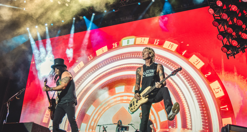 Palco de grande show de rock iluminado com multidão durante apresentação do Guns N’ Roses