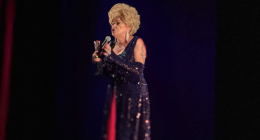 Nany People no palco durante espetáculo de humor com iluminação cênica e público ao fundo