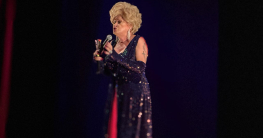 Nany People no palco durante espetáculo de humor com iluminação cênica e público ao fundo