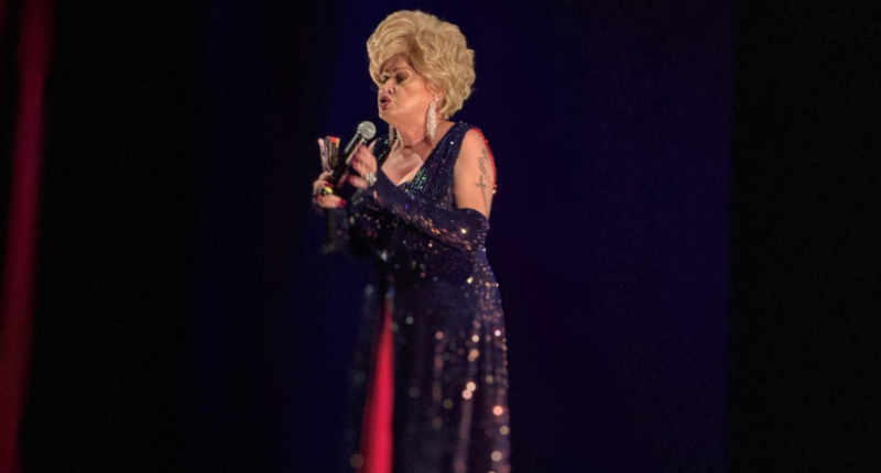 Nany People no palco durante espetáculo de humor com iluminação cênica e público ao fundo