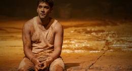 Cena teatral intensa com atores em palco coberto por lama durante espetáculo Tom na Fazenda