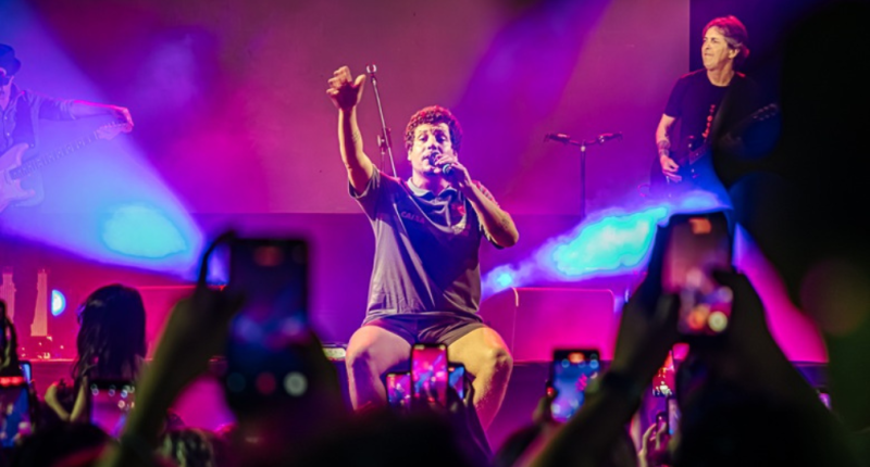 Cantor Chico Chico no palco com público participando em coro durante show noturno em Campo Grande