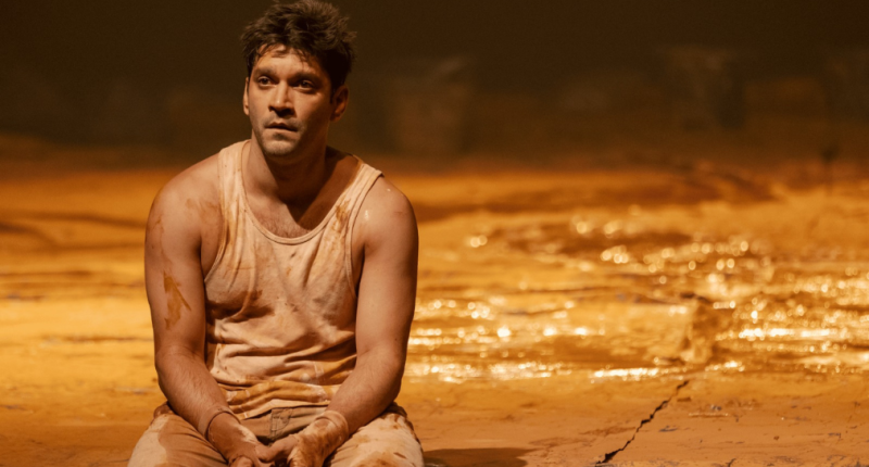 Atores em cena com corpos cobertos de lama em palco escuro transmitindo tensão e intensidade dramática