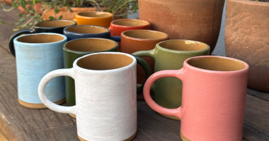 Peças de cerâmica artesanal expostas em mesas com público circulando em feira cultural em cafeteria