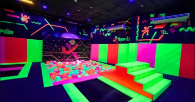 Crianças brincando em parque de trampolins indoor com ambiente colorido e equipe auxiliando famílias