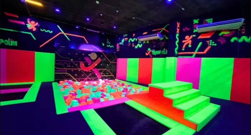 Crianças brincando em parque de trampolins indoor com ambiente colorido e equipe auxiliando famílias
