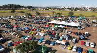 Carros antigos expostos durante encontro automotivo com público reunido em Campo Grande ao entardecer.