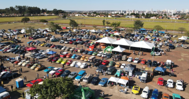 Carros antigos expostos durante encontro automotivo com público reunido em Campo Grande ao entardecer.