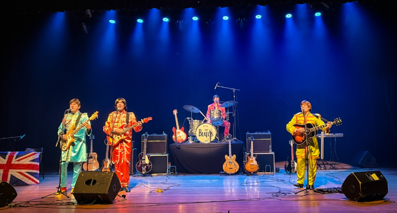banda tributo Beatles em palco com figurinos clássicos e iluminação de show ao vivo