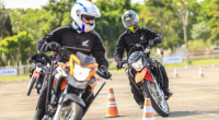 motociclistas participando de curso prático de pilotagem segura em circuito com cones e instrutor orientando