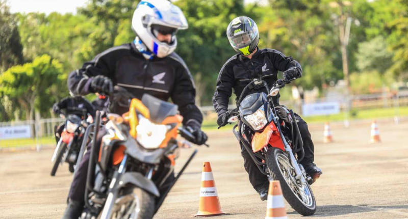 motociclistas participando de curso prático de pilotagem segura em circuito com cones e instrutor orientando