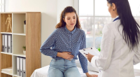 mulher sentada sozinha em ambiente fechado segurando a barriga em expressão de dor e desconforto intestinal