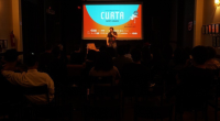 diretor conversa com público durante festival de cinema em auditório com projeção de curta-metragem