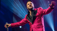 Maurício Manieri canta no palco durante apresentação da turnê “Classics – Inesquecível Tour”, cercado por iluminação intimista e clima nostálgico