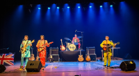Banda tributo aos Beatles se apresenta em palco com figurinos clássicos inspirados no quarteto de Liverpool e iluminação de show.