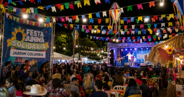 Famílias circulam entre barracas típicas durante festa junina comunitária, enquanto apresentações culturais acontecem em palco ao ar livre.