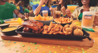 Grupo de amigos assiste a uma partida de futebol enquanto compartilha pratos do Outback, bebidas e momentos de confraternização em ambiente descontraído.