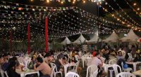 Barracas de comidas típicas, bandeirinhas coloridas e público durante o Arraiá Beneficente realizado no Norte Sul Plaza.