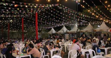 Barracas de comidas típicas, bandeirinhas coloridas e público durante o Arraiá Beneficente realizado no Norte Sul Plaza.