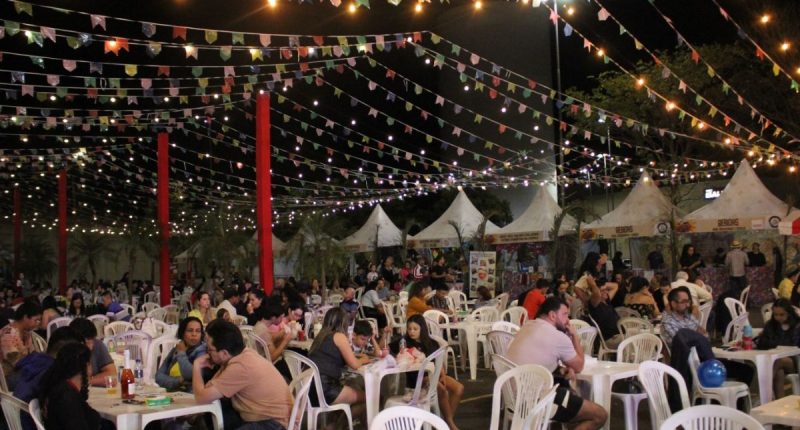 Barracas de comidas típicas, bandeirinhas coloridas e público durante o Arraiá Beneficente realizado no Norte Sul Plaza.
