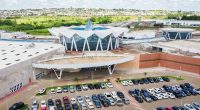 Vista aérea do Bosque dos Ipês, em Campo Grande, mostrando a estrutura externa do shopping e seu estacionamento.