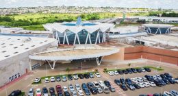Vista aérea do Bosque dos Ipês, em Campo Grande, mostrando a estrutura externa do shopping e seu estacionamento.