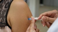 Profissional de saúde aplicando vacina no braço de adolescente em unidade de vacinação.