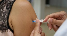 Profissional de saúde aplicando vacina no braço de adolescente em unidade de vacinação.